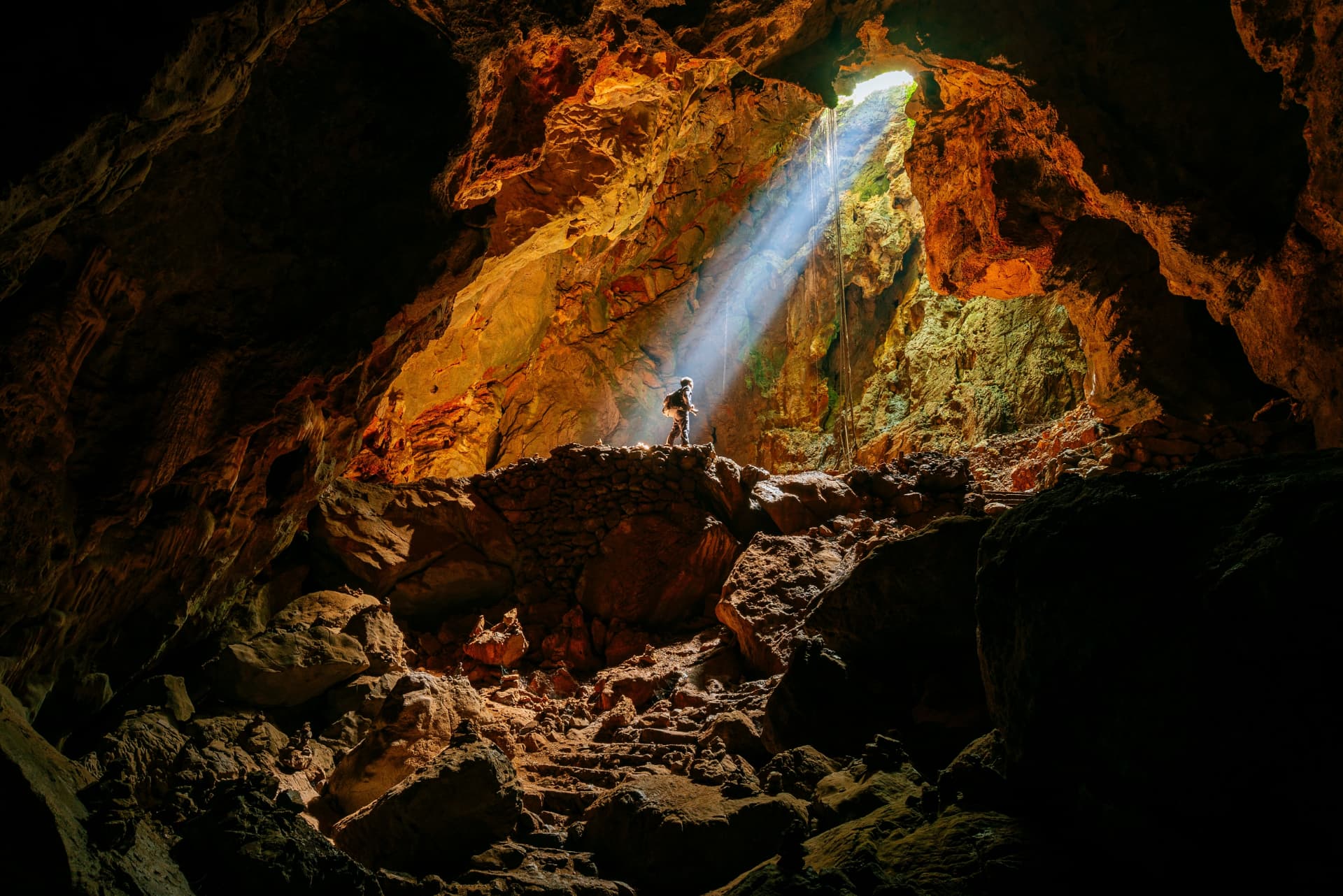 Explorer in a cave lit by a shaft of daylight
