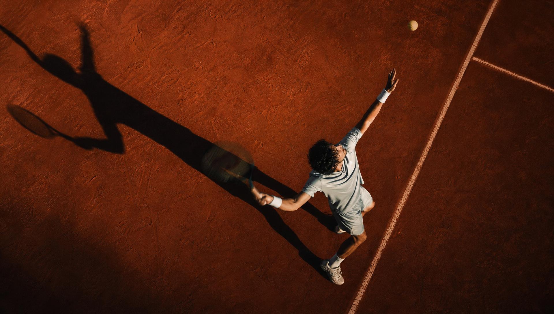 Tennis player serving on a clay court at golden hour, symbolising precision, momentum and timing